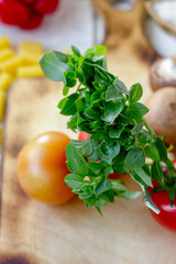 Green basil leaves on kitchen board with vegetables.