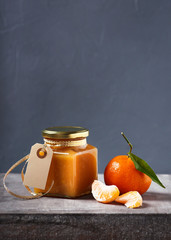 Tasty mandarin jam in a glass jar on dark grey background. Copy space.  