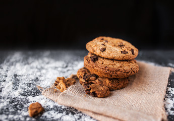 Chocolate chip cookies on dark background  withmelted  flour place for text. Choco cookie on  linen napkin on black slate board, selective focus with copyspace