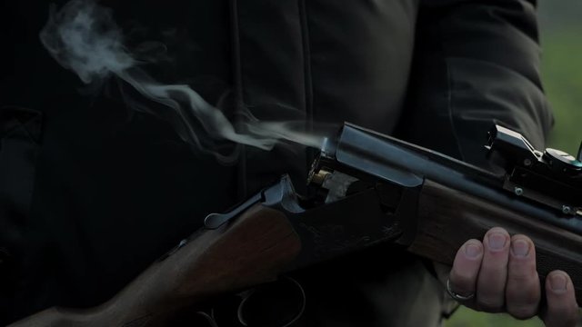 Impressive closeup shot of sportsman hands takes out a cartridge in a vertical double barrel shotgun outdoors. Slow motion.
