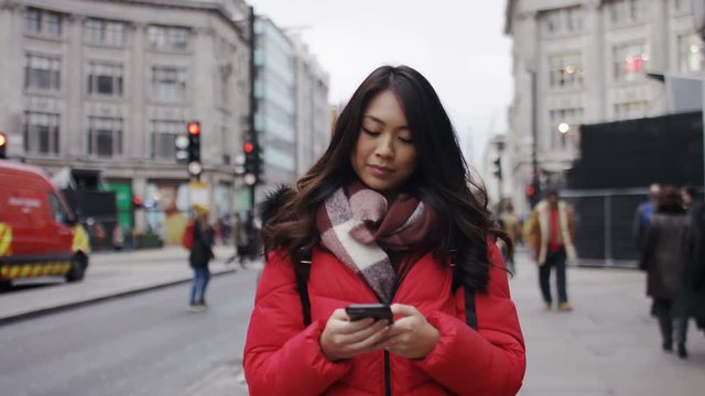 Attractive young woman walks along the street whilst using her phone, in slow motion