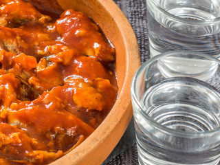 Sprat in tomato sauce in a ceramic dish and two glasses of vodka on a black background. Canned fish.