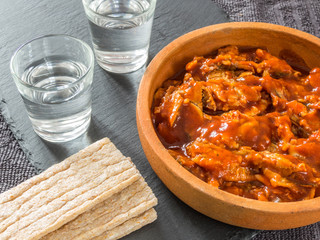 Sprat in tomato sauce in a ceramic dish, two glasses of vodka on a black background and crispbread. Canned fish.