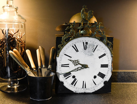 Old clock with silverware and vanilla jar in a black kitchen