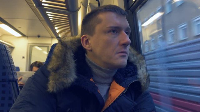 Sad man in a park jacket travels by train, looking out the window