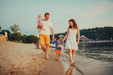 concept family beach vacation. Family of four people mom, dad and brothers children boys walking, want barefoot on the river bank by the hand at sunset in the summer