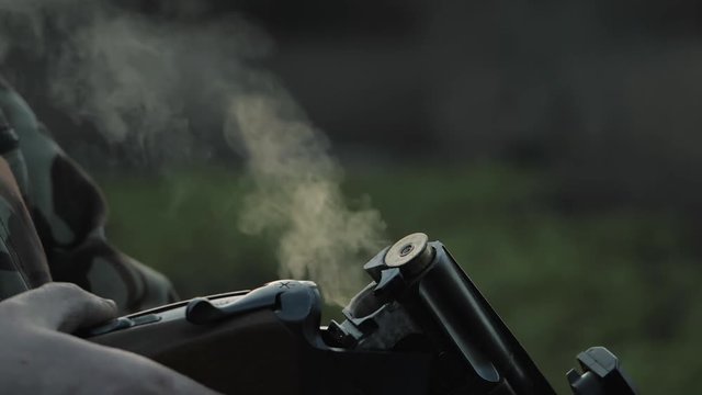 Sports shooting. Hunter in camouflage reloading cartridge. Smoke from the trunks of smooth-bore hunting rifle after firing. Slow motion.