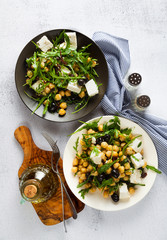 two plates of vegetable salad with chickpeas, arugula, feta cheese or tofu and black olives on a natural stone background. healthy eating