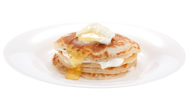 Serving pancakes with sour cream and honey on the plate. Isolated on white background.