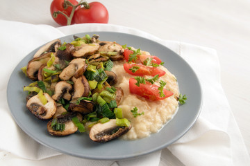 mushrooms and leek with parsnip puree and tomatoes on a gray plate, white napkin on a white table with copy space, healthy vegetarian diet meal from organic vegetables
