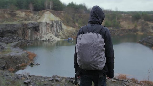 Walking into the wild nature in the rain near flooded quarry and basalt pillars, tourist, trekker, view from behind, slow motion