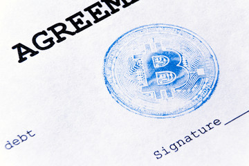 Macro. Blue stamp of virtual currency bitcoin on a loan agreement. The loan agreement, the signature is printed on a white sheet of paper.