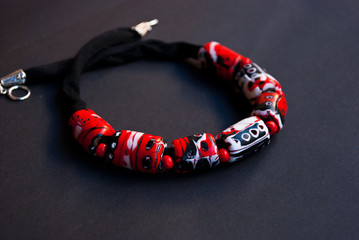 Fototapeta premium Handmade jewelry from polymer clay. Beautiful bright necklace on black background. Fashion foto. Bijouterie in macro. Black and red collar.