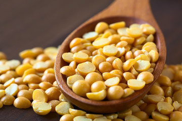 Raw yellow split peas in wooden spoon, photographed on dark wood with natural light (Selective...