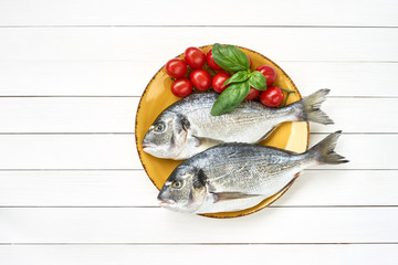 Fresh dorado fish on yellow plate with tomatoes on white wooden table. Top view, copy space.