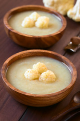 Blumenkohlcremesuppe mit Blumenkohlröschen und gemahlenen Muskatnuss, fotografiert mit natürlichem Licht (Selektiver Fokus, Fokus auf die ersten Blumenkohlröschen auf der vorderen Suppe)