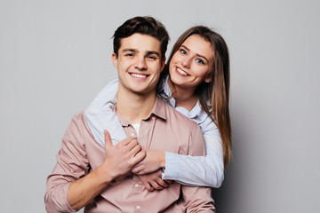 Portrait of a cheerful young couple hugging while standing and looking at camera over gray