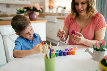 Young mother and her son having fun while painting eggs for Easter