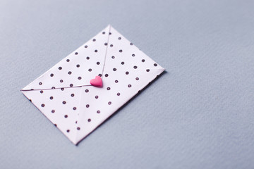 White dotted envelope with pink heart shaped figure. Hand crafted love letter for Saint Valentines Day celebration. Celebrate 14 February with handmade postcard. Send post cards to people you love
