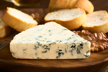 Blue cheese with walnuts and bread slices on wooden plate, photographed with natural light...