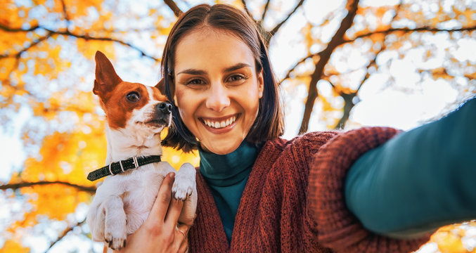 Portrait of smiling young woman with dog outdoors in autumn making selfie