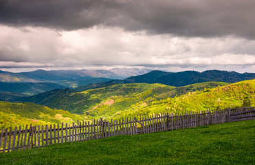 Naklejka premium wooden fence along the grassy hillside. beautiful springtime landscape of Carpathian mountains on a cloudy day. 