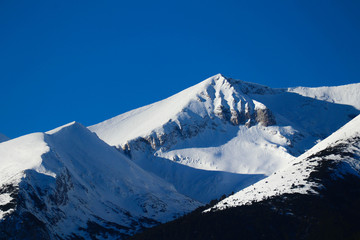 Mountain snow peak, beautiful natural winter backdrop. Ice top of the hill, blue sky background. Alpine landscape.