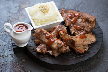Baked sliced pork ribs with potato puree and sauce on a black wooden serving board, studio shot