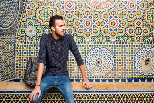 Young Muslim man sitting with traditional Moroccan decoration in background