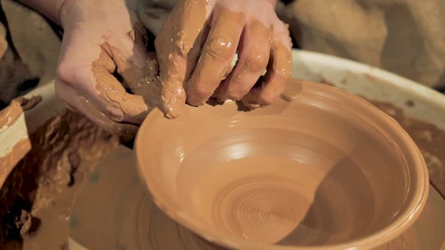 Potters hands form an edge of a bowl on a wheel. 