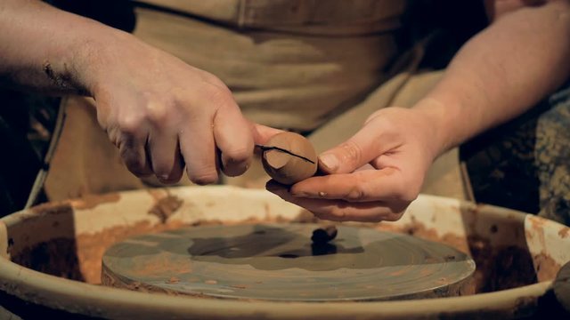 A potter cuts off excess clay from a spoon workpiece. 