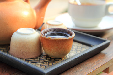 close up earthenware teapot with pouring hot tea in a brown cup are placed on the table for healthy drinking in morning time