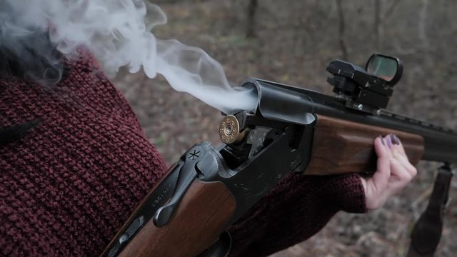 Hunter woman in burgundy warm clothes takes out cartridges from a gun. Smoke from the trunks of smooth-bore hunting rifle after firing. Slow motion.