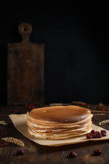 a pile of pancakes, berries, biscuits and a cutting board on parchment on a dark wooden table