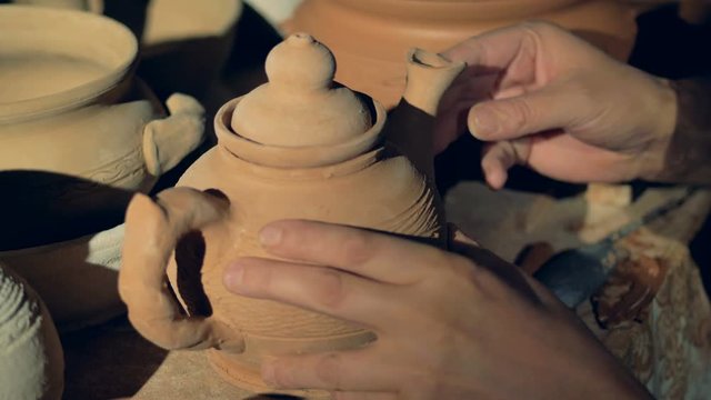 A potter inspects a teapot spout before firing. 