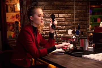 blonde in  burgundy style suit 80s dials  number on retro phone in bar
