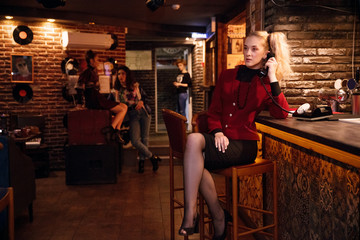 Fototapeta na wymiar young woman in burgundy business suit of style 80s talking on retro phone at bar counter