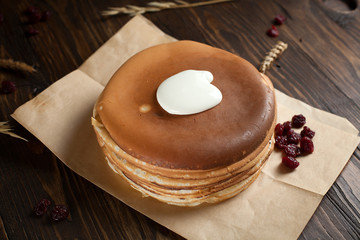 a pile of pancakes, berries, cookies, sour cream and a cutting board on parchment on a dark wooden table