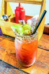 Caesar or bloody mary cocktail drink rimmed with spice and garnished with lime wedge, pepper, and olives on a hot summer day.