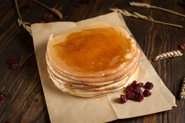 a pile of pancakes, berries, cookies, butter and a cutting board on parchment on a dark wooden table