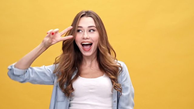 Funny brunette woman in denim shirt dancing and looking at the camera over yellow background