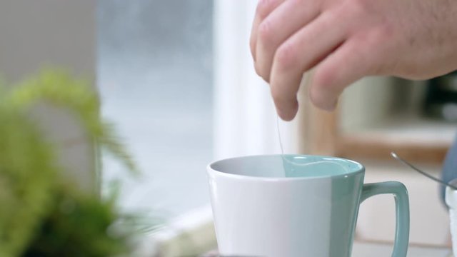 Tracking shot of tea bag bobbing in teal mug of steaming hot water