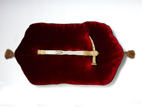 Antique pickax resting on red velvet cushion, white background 