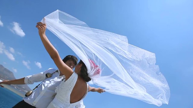 bride and groom stand on a strong wind at the wedding day near the sea. Veil brides beautifully fluttering in the wind. Greece.