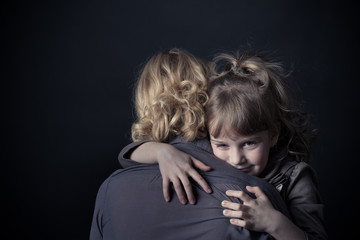 Photo shooting indoors. On a black background. Child ( girl ) hugs his mother.
