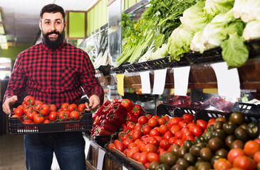 Male seller showing fresh tomatoes in vegetables shop