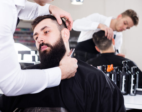 Adult stylist creating shape for beard of client