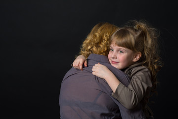 Photo shooting indoors. On a black background. Child ( girl ) hugs his mother.
