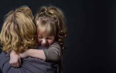 Photo shooting indoors. On a black background. Child ( girl ) hugs his mother.
