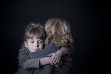 Photo shooting indoors. On a black background. Child ( girl ) hugs his mother.
